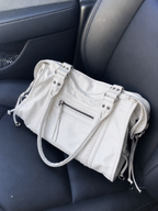 White - A light beige faux-leather shoulder bag with silver hardware, resting on a dark gray car seat.